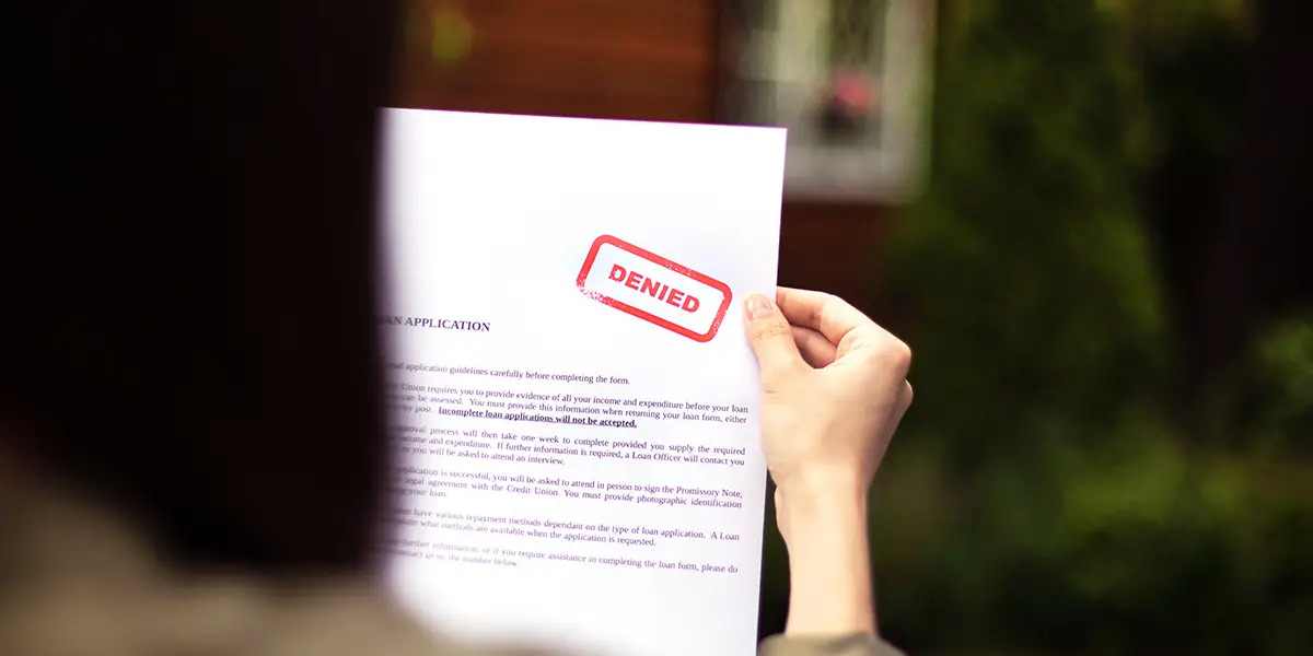 Photo of a woman holding up her apartment application, with a red stamp that says "DENIED."