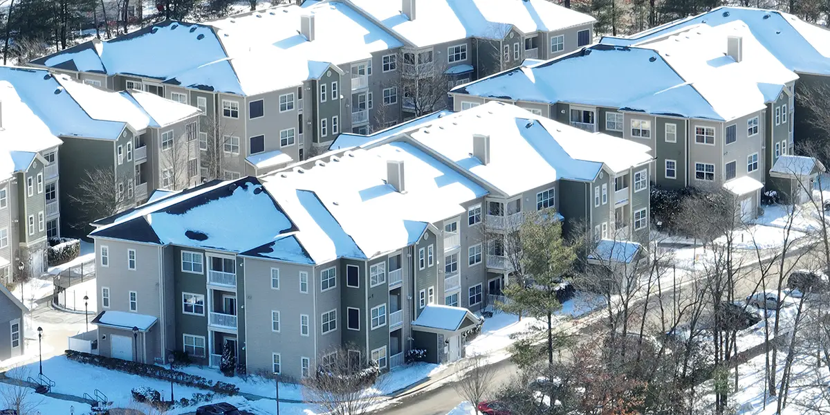 Aerial photo of an apartment community during the wintertime. Trees are bare, and snow is on the ground and on the roof of the apartment buildings.